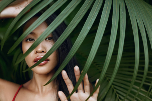 Beauty. Beautiful asian woman with palm leaf over face in nature - Fotografie, Obrázek