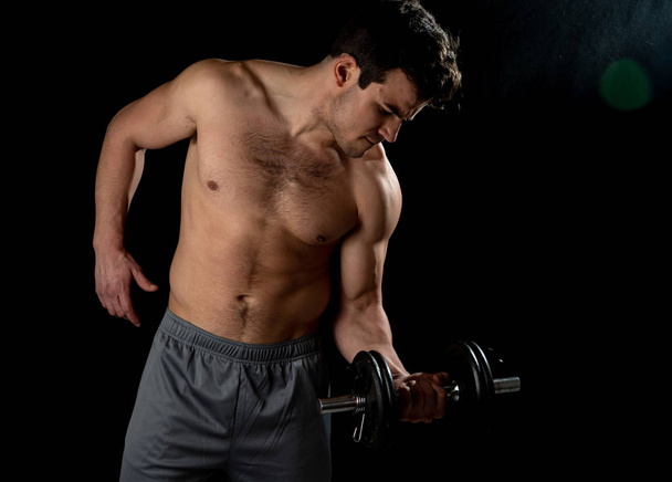 Portrait of young muscular built athlete man working out doing exercises and posing with dumbbells, bodybuilder male naked torso lifting weights in Fitness sports Body care and healthy lifestyle. - 写真・画像