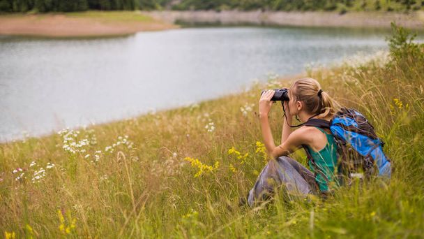 Woman hiker using binoculars while spending time in the beautiful nature. - Photo, image