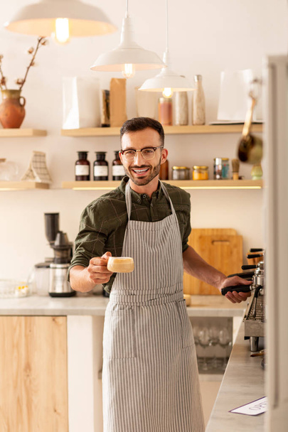Cheerful handsome barista welcoming guests and making coffee - Fotó, kép