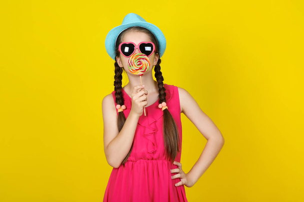 Beautiful young girl with sweet lollipop on yellow background - Фото, изображение