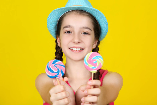 Beautiful young girl with sweet lollipops on yellow background - 写真・画像