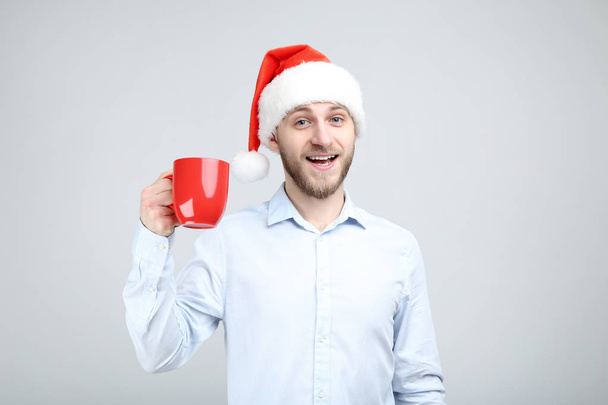 Portrait of young man with santa hat and red cup on grey backgro - Foto, afbeelding