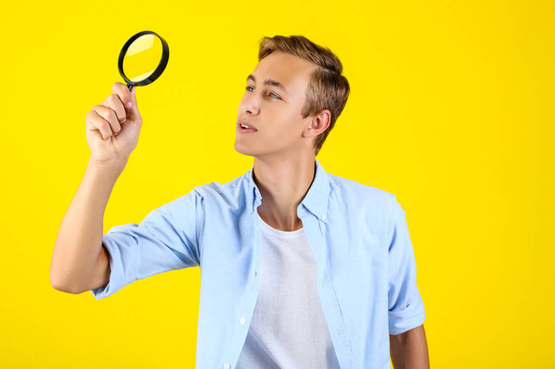 Young man with magnifying glass on yellow background - Photo, image