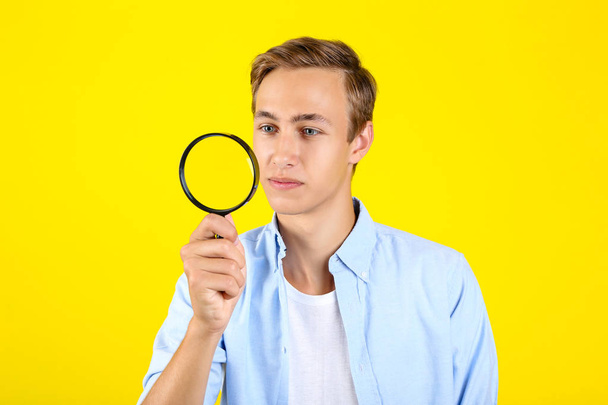 Young man with magnifying glass on yellow background - Photo, image