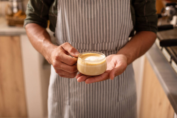 Barista cappuccino fincan tutan çizgili önlük giyiyor - Fotoğraf, Görsel