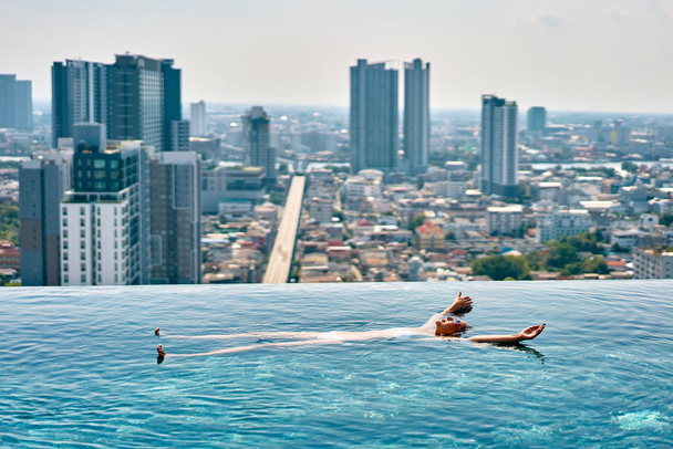 Young woman relaxing in rooftop swimming pool and floating in water - Photo, Image
