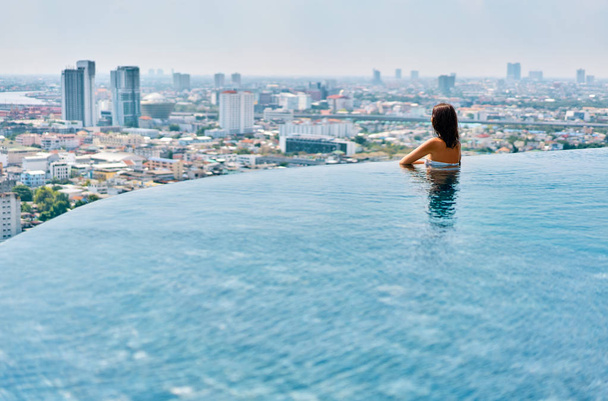 rear view of woman relaxing at edge of rooftop swimming pool - Photo, Image