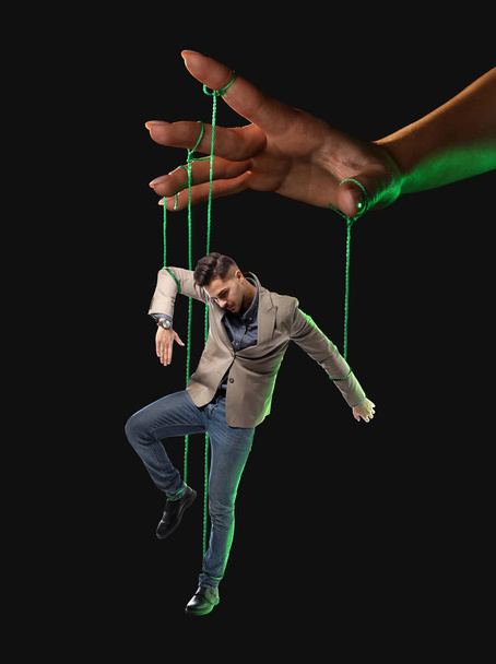 Hand van poppenspeler manipuleren van de mens als marionet op donkere achtergrond - Foto, afbeelding