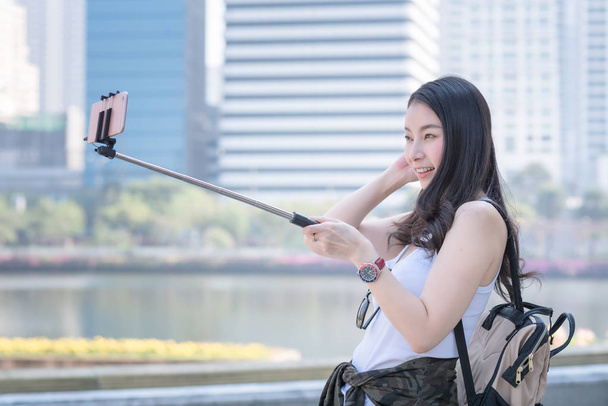 Hermosa mujer turista asiática tomando selfies en un teléfono inteligente en el centro urbano de la ciudad
 - Foto, Imagen