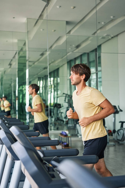 Young sportsman running on treadmill at gym doing workout - Foto, afbeelding