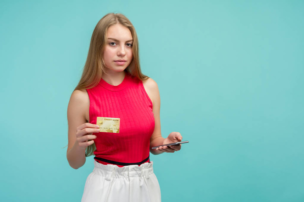 Portret van een opgewonden jong meisje tonen plastic creditcard terwijl het houden van mobiele telefoon - Foto, afbeelding