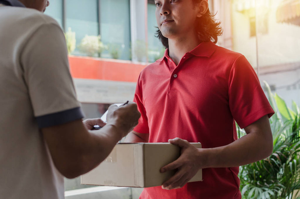 home delivery service man in red uniform and young man customer appending signature in digital mobile phone receiving parcel post box from courier at home, express delivery, online shopping concept - Fotoğraf, Görsel