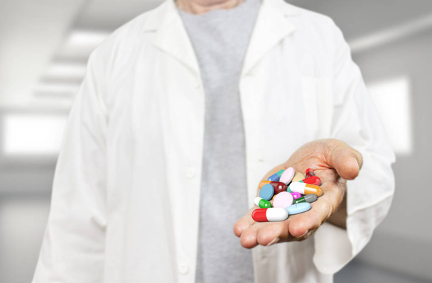 Old doctor holding pills, capsules, drugs and medics on a blurred hospital background 3d rendering. Medicine, health care, overmedication and disease healing concept. - Photo, Image