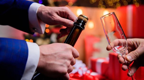 シャンパンやスパークリングワインを飲む。シャンパンで新年を祝います。手はシャンパンボトルを開き、ガラスのクリスマスの装飾の背景を保持します。新年の直前新年のカウントダウン - 写真・画像