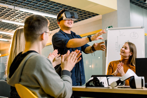 Zespół biznesowy z wielu rasowych ludzi pracujących w wirtualnej rzeczywistości aplikacji i gier, młody podekscytowany człowiek testowania okulary VR lub okulary stojące w biurze z kolegami - Zdjęcie, obraz