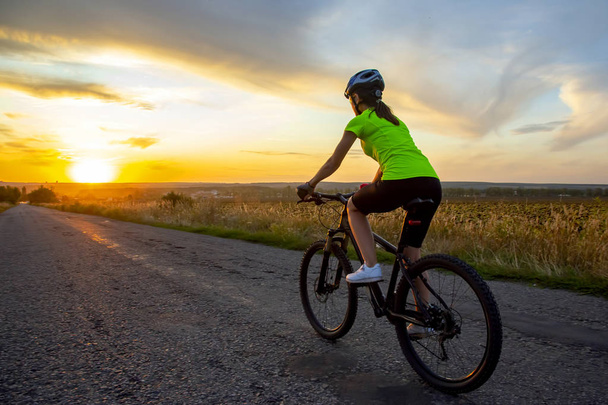 Όμορφο κορίτσι ποδηλάτης ιππασία ένα ποδήλατο στο δρόμο προς τον ήλιο - Φωτογραφία, εικόνα