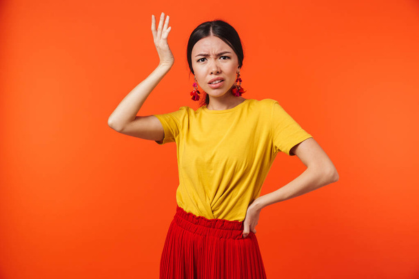 Confused displeased young woman posing isolated over orange wall background. - Foto, afbeelding