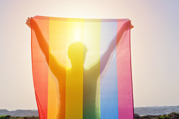 Nuori nainen nostaa kätensä heiluttaen LGBT sateenkaaren lippua
 - Valokuva, kuva