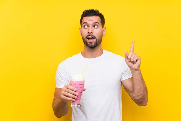 Young man with strawberry milkshake over isolated yellow background intending to realizes the solution while lifting a finger up - Valokuva, kuva