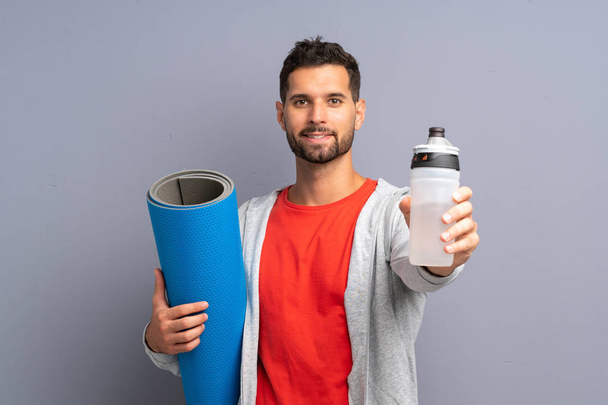 Молодий спортивний чоловік з килимом і з пляшкою води
 - Фото, зображення