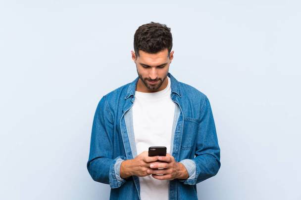Bonito homem sobre fundo azul isolado enviando uma mensagem com o celular - Foto, Imagem
