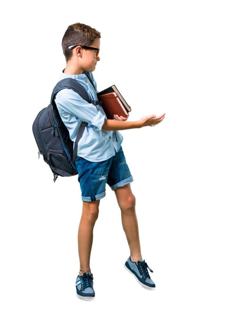 Cuerpo completo de Student boy con mochila y gafas apuntando hacia atrás con el dedo índice sobre fondo blanco aislado
 - Foto, Imagen