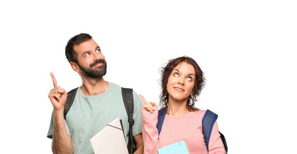Two students with backpacks and books pointing with the finger a great idea and looking up on isolated white background - 写真・画像