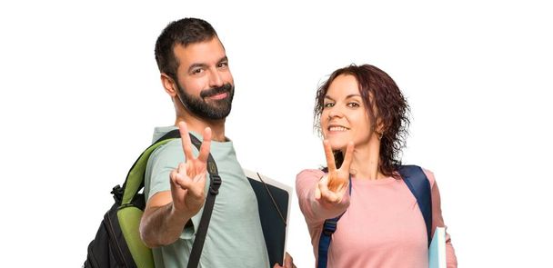 Two students with backpacks and books smiling and showing victory sign on isolated white background - Photo, Image