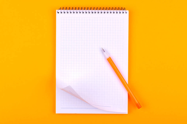 Блокнот на пружині з білими аркушами паперу для малюнків, текстів і нотаток, поруч з жовтою ручкою лежить на помаранчевому фоні
 - Фото, зображення