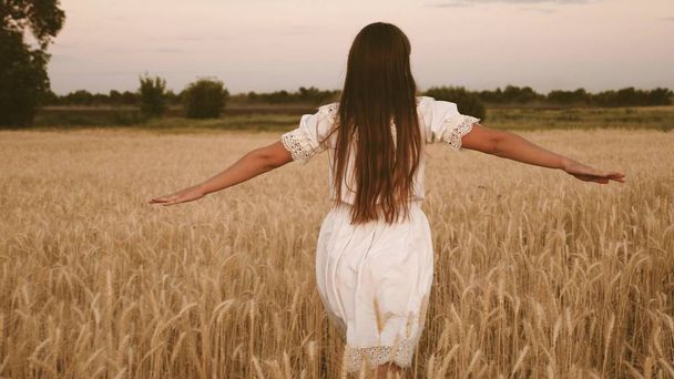 Девушка путешествует в поле. концепция экотуризма. счастливая девушка идет по полю желтой пшеницы и своими руками касается колосьев пшеницы. Медленное движение
. - Фото, изображение