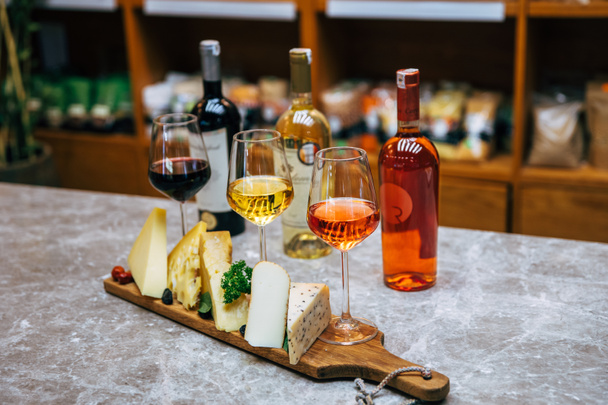 Ένα μπουκάλι κρασί και τυρί. Ποικιλία ή διάφορα είδη τυριού, μπουκάλι κρασιού και γυαλιά στο τραπέζι στο εστιατόριο. Κόκκινα ποτήρια κρασιού και μπουκάλι στο τραπέζι. Εικόνα οινοποιίας - Φωτογραφία, εικόνα