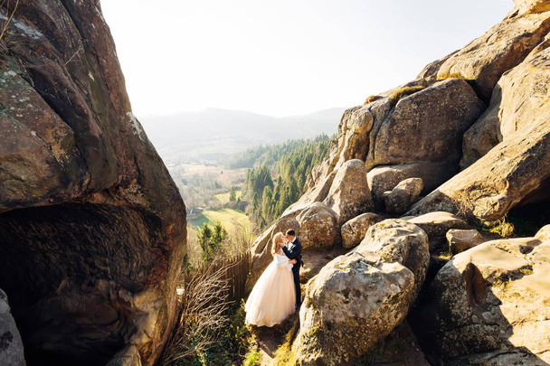 Νιόπαντροι φιλιούνται σε γκρεμό με θέα τα βουνά. Έννοια  - Φωτογραφία, εικόνα
