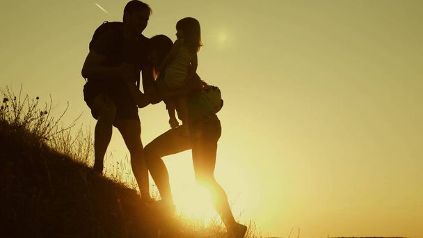 Isä ojentaa kätensä auttaakseen lapsia kiipeämään vuorelle. Turistien perhe, jonka lapset matkustavat auringonlaskun aikaan. Isä, lapset ja äiti reput matkustaa kiivetä vuorelle auringossa. matkailutiimityöskentely
 - Valokuva, kuva