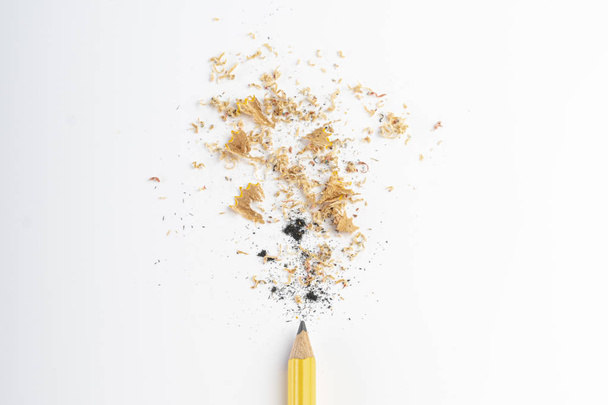 Niedawno zaostrzony ołówek z wiórów drewnianych i kopalni na białym stole. Ołówek żółty - Zdjęcie, obraz