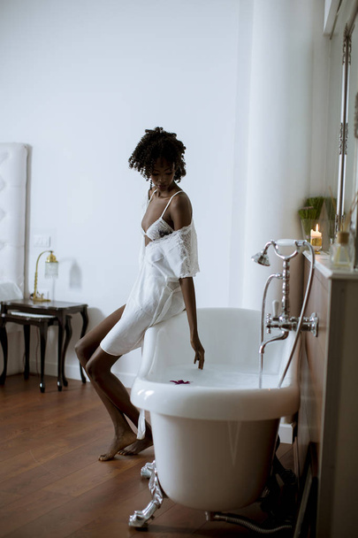 浴室のバスタブのそばに立つかなり若いアフリカ系アメリカ人女性 - 写真・画像