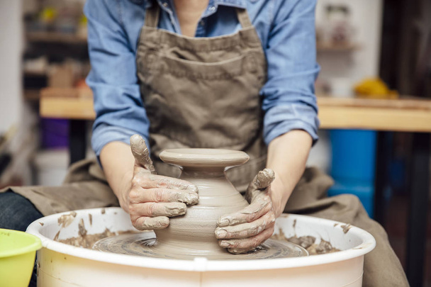 Alfarera senior de buen aspecto trabajando en rueda de cerámica mientras está sentada en su taller
 - Foto, Imagen