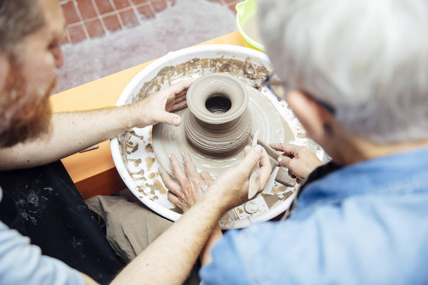 Vue sur la femme âgée tournant de l'argile sur une roue avec l'aide d'un professeur à la classe de poterie
 - Photo, image