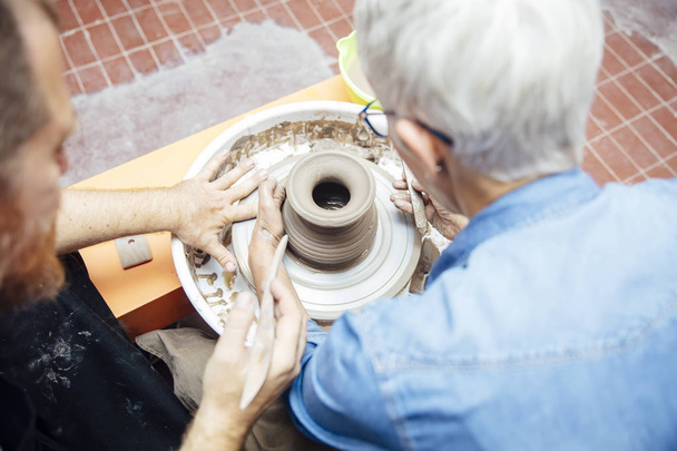 Nad widokiem na starszy kobieta przędzenia gliny na kole z pomocą nauczyciela w klasie ceramiki - Zdjęcie, obraz