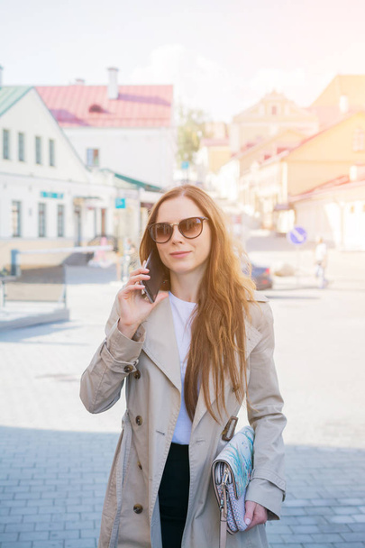 stylish young woman is walking on the street and sms typing on the phone - Valokuva, kuva