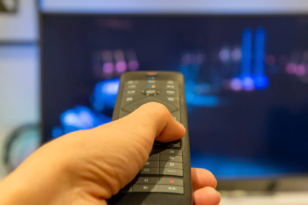 Hand holding TV remote control with a television in the background. Close up - Photo, Image