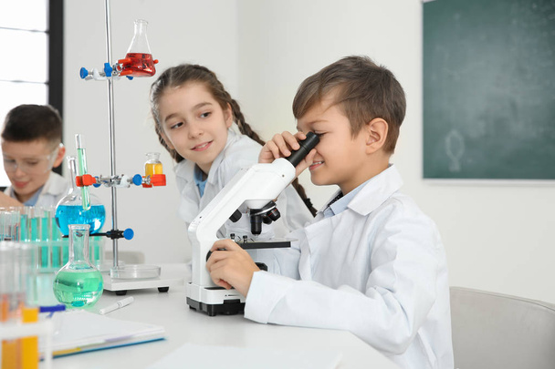 Schoolboy looking through microscope and his classmates at chemistry lesson - Foto, Imagem