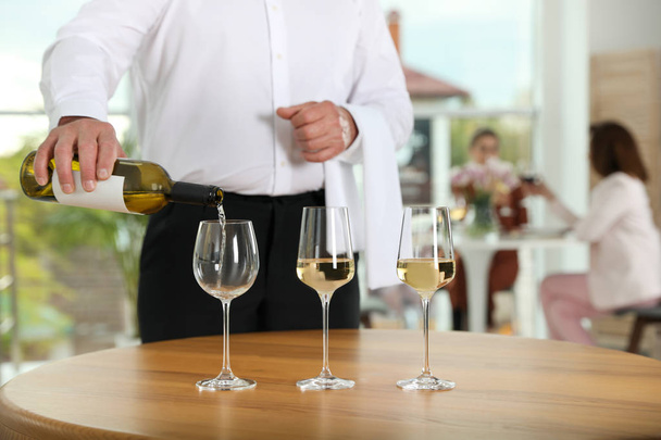 Waiter pouring wine into glass in restaurant, closeup - Фото, изображение