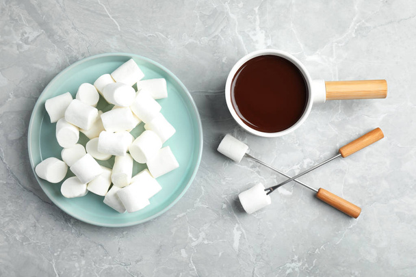 Fondue pot with dark chocolate and marshmallows on marble table, flat lay - Фото, изображение