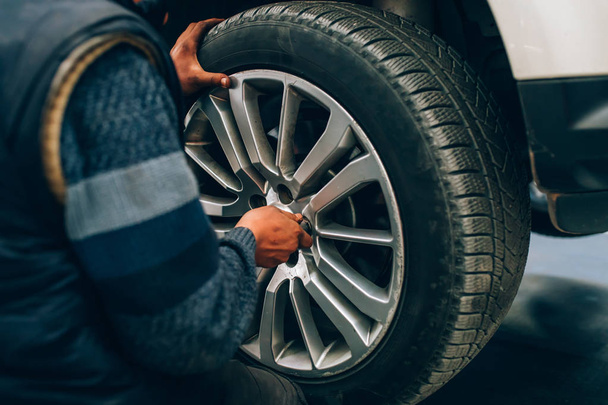 Mechanician mudando roda de carro na oficina de reparação de automóveis. Mecânico ajustando a roda do pneu usando mão e ferramenta na garagem do carro de reparação
 - Foto, Imagem