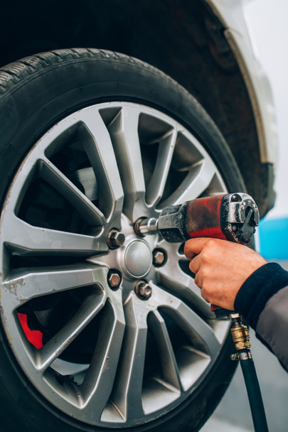 Mechanician mudando roda de carro na oficina de reparação de automóveis. Mecânico ajustando a roda do pneu usando mão e ferramenta na garagem do carro de reparação
 - Foto, Imagem