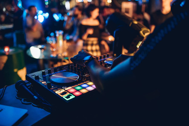 DJ speelt live set en het mixen van muziek op draaitafel console op het podium in de nachtclub. Disc Jokey Hands op een geluidsmixer station op clubfeest. DJ mixer controller paneel voor het afspelen van muziek en feesten. - Foto, afbeelding