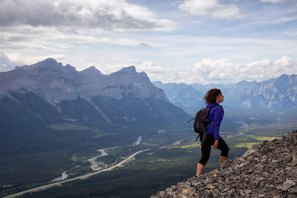Adventurous Girl is hiking up a rocky mountain during a cloudy and rainy day. Taken from Mt Lady MacDonald, Canmore, Alberta, Canada. - Фото, зображення