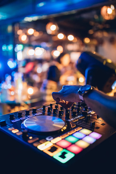 DJ gra na żywo i miksuje muzykę na konsoli gramofonu na scenie w klubie nocnym. Disc Jokey Hands na stacji mikserskiej na imprezie klubowej. DJ mikser panel kontrolny do odtwarzania muzyki i imprezowania. - Zdjęcie, obraz