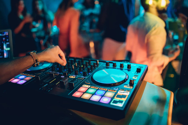 DJはナイトクラブのステージでターンテーブルコンソールでライブセットとミキシング音楽を演奏します。ディスクジョッキークラブパーティーでサウンドミキサーステーションに手。音楽やパーティーを再生するためのDJミキサーコントローラーパネル. - 写真・画像